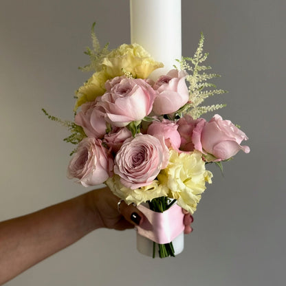 Bouquet of pink and yellow flowers with a white candle held by a hand against a gray background