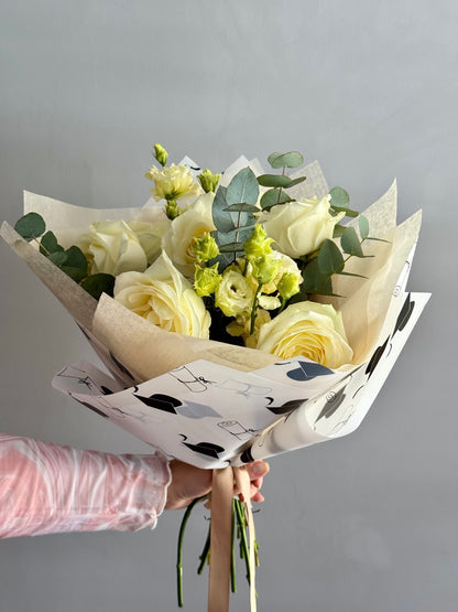 Bouquet of white and green flowers wrapped in paper with black patterns, held by a person.